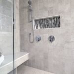 How To Increase the Water Pressure in Your Home’s Shower A gray-tiled walk-in shower contains a bench with a white towel and a gray washcloth. There's a window in the shower.