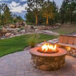 A fire bit is blazing with flames, there is a semi-circular bench stretching around the fire pit. There are trees in the background.