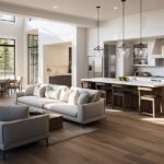 A modern, open-concept dining room and kitchen decorated with beige, gray, and white furniture with brown hardwood flooring.