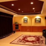 Three leather recliners sit on a red oriental rug in a home theater with recessed lighting and a velvet curtain.