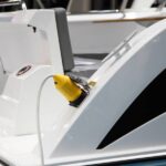 Electric Boat Battery: Factors To Consider A white electric boat sits in the marina, receiving an electric charge from a bright yellow charger.