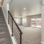 A carpeted staircase that leads down into a beautiful, open-concept basement with recessed overhead lighting.