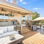 A backyard deck with a wooden table and a couch with gray cushions. It is a bright, partly cloudy day.