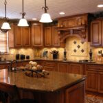 An expensive-looking Tuscan-style kitchen with dark cabinets and countertops, black appliances, and an intricate tile backsplash.