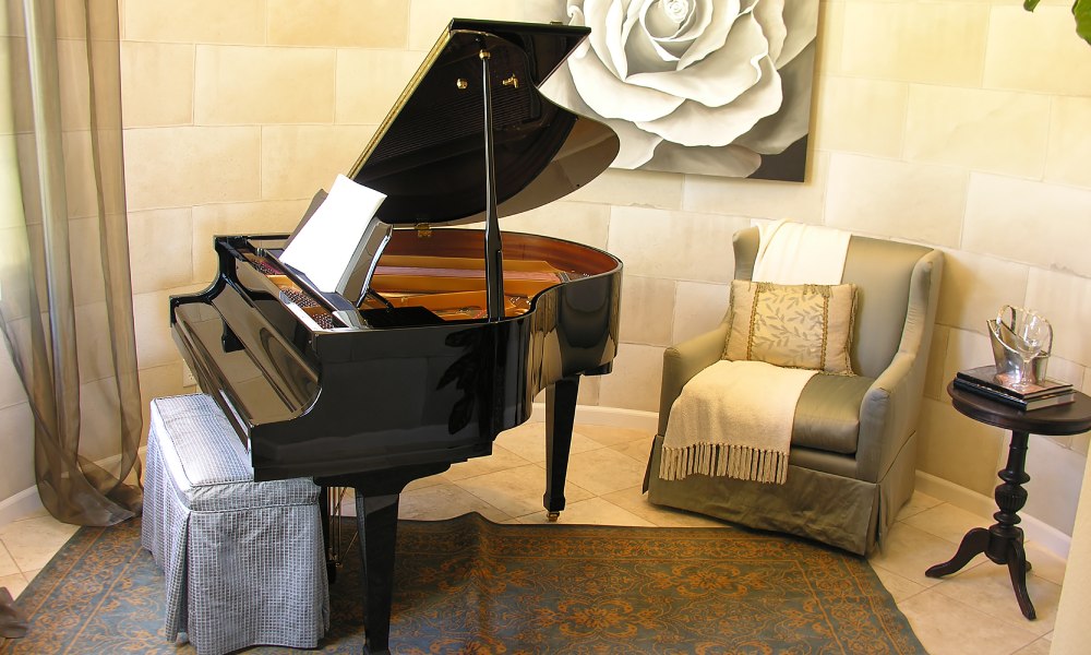 A grand piano sits in a rounded part of a room with other furniture and accessories, including a rose painting behind it.