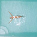 An overview of a woman wearing a white bathing suit set, relaxing in clear pool water on a hot, sunny day.