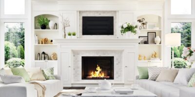 A luxurious home living room with a large fireplace in the center surrounded by white accents, decor, and furniture.