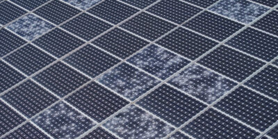 An aerial view of a large solar panel. Several individual cells on the panel are cracked from hail damage.