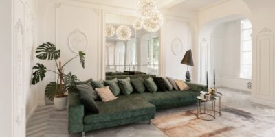 A green couch faces forward with a mirror behind it, set against white walls and gray parquet flooring with a brown rug.