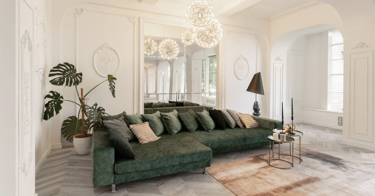 A green couch faces forward with a mirror behind it, set against white walls and gray parquet flooring with a brown rug.