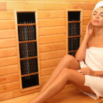 Advantages of Having an Infrared Sauna in Your Home A woman with a white towel wrapped around her body and a white towel wrapped around her head sits in a sauna.