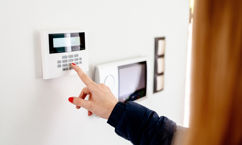 A woman with red hair using her finger to enter a security code on a white keypad mounted on a wall.