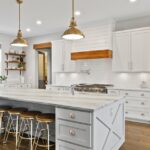A wide view of a modern farmhouse kitchen, including white cabinetry, a large white counter island, and open shelving.