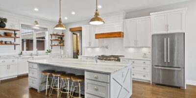 A wide view of a modern farmhouse kitchen, including white cabinetry, a large white counter island, and open shelving.