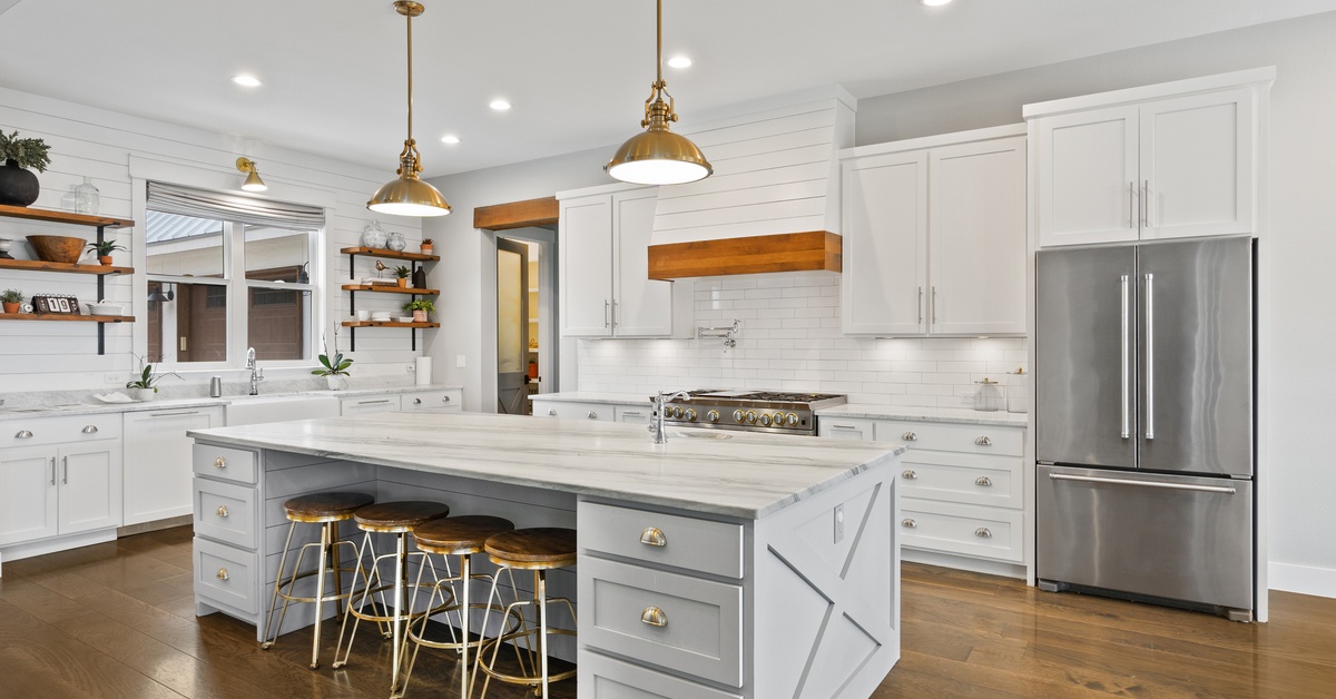 A wide view of a modern farmhouse kitchen, including white cabinetry, a large white counter island, and open shelving.