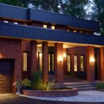 Effective Waterproofing Solutions for Flat Roofs Front of a red brick home at twilight with a pond and stone porch. Lamps illuminate the flat roof house with trees in the background.